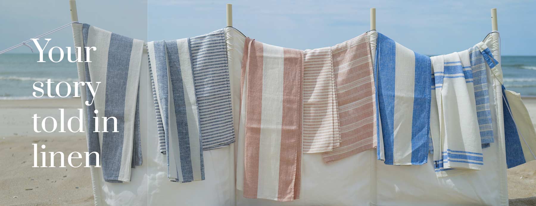 Your story told in linen – blue, grey and pink striped linen beach towels drying beside the sea.