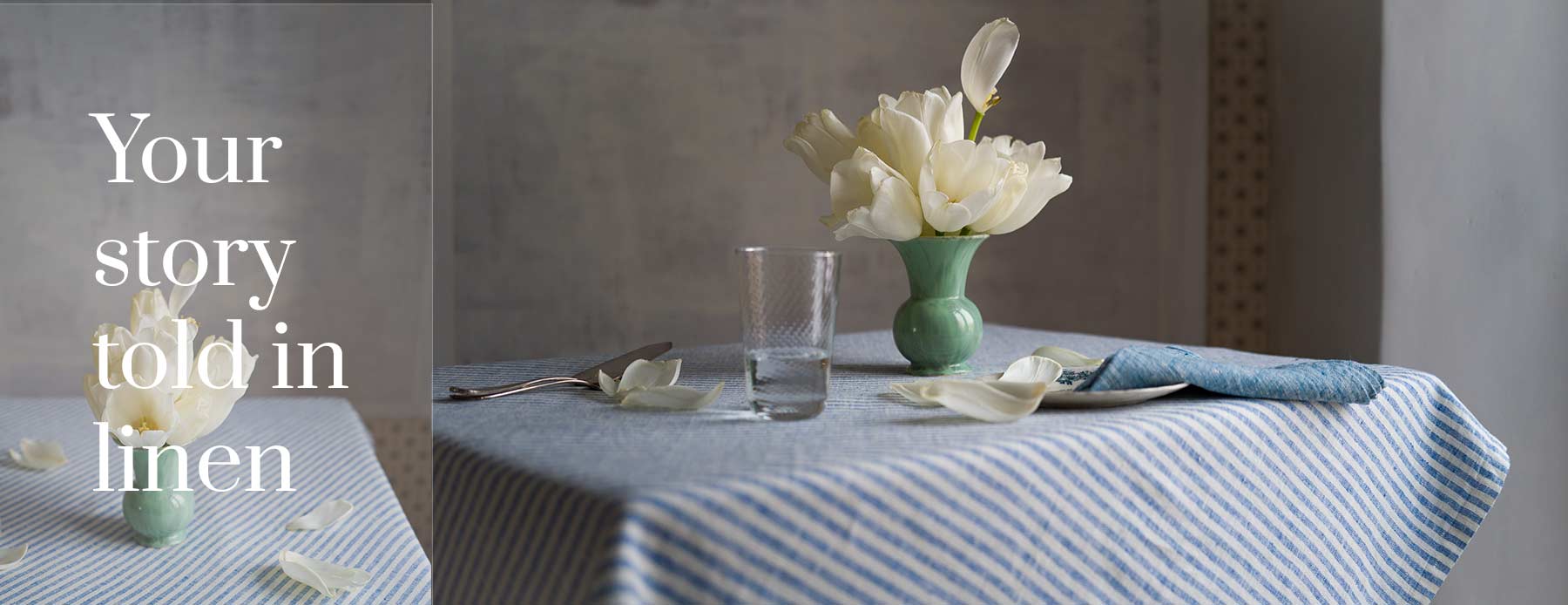 Your story told in linen – blue striped linen tablecloth and napkin with white tulips in a green vase.