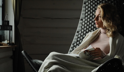 Woman reading under a wool throw by a window